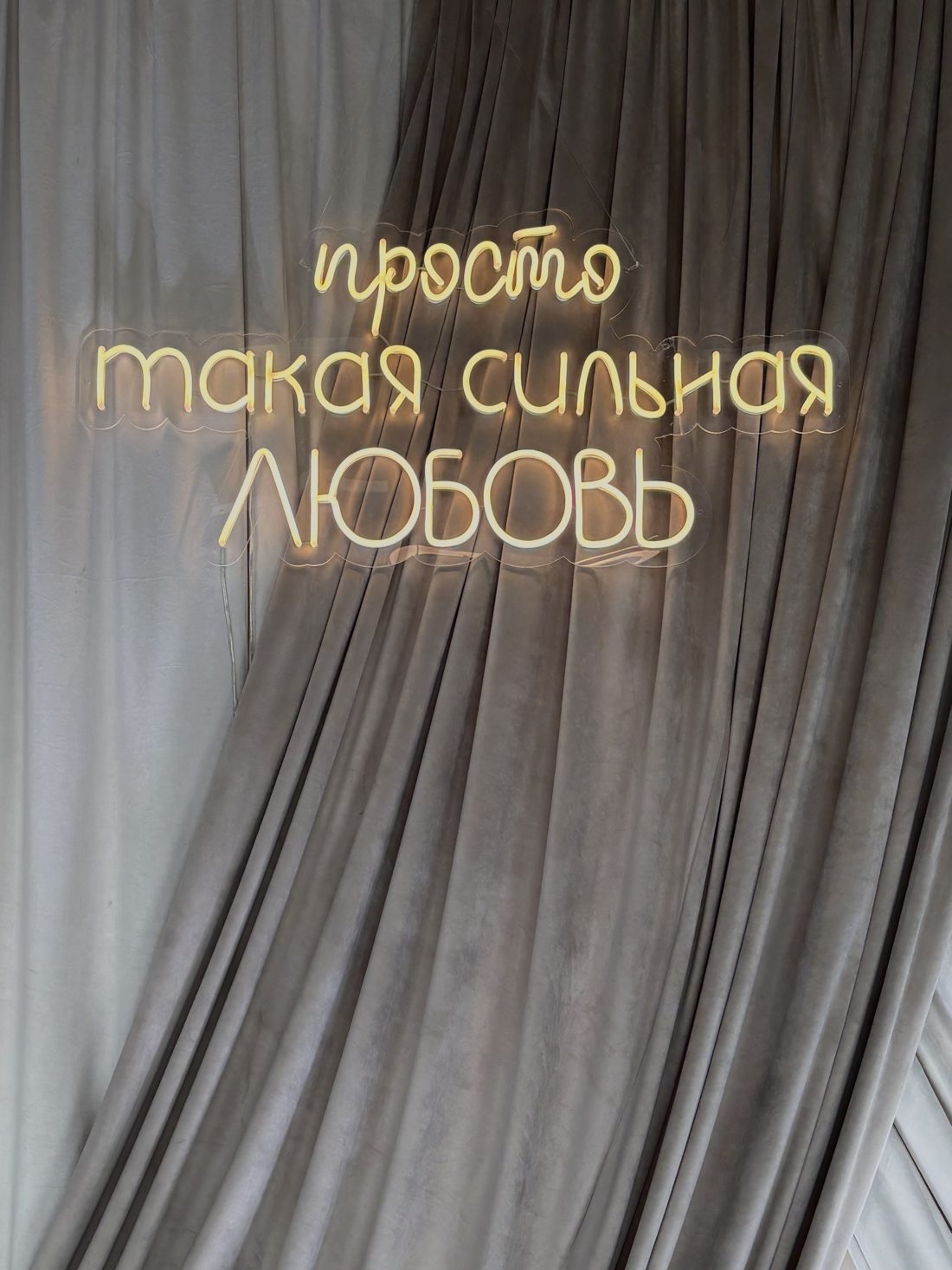 Неоновая надпись «просто такая сильная любовь» на фоне драпировки